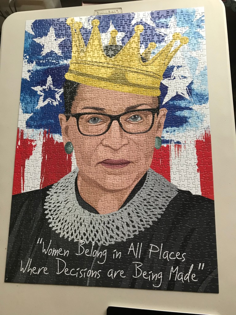 Finished jigsaw puzzle of Ruth Bader Ginsburg image in front of American flag with text written at bottom that says "Women belong in all places where decisions are being made." 