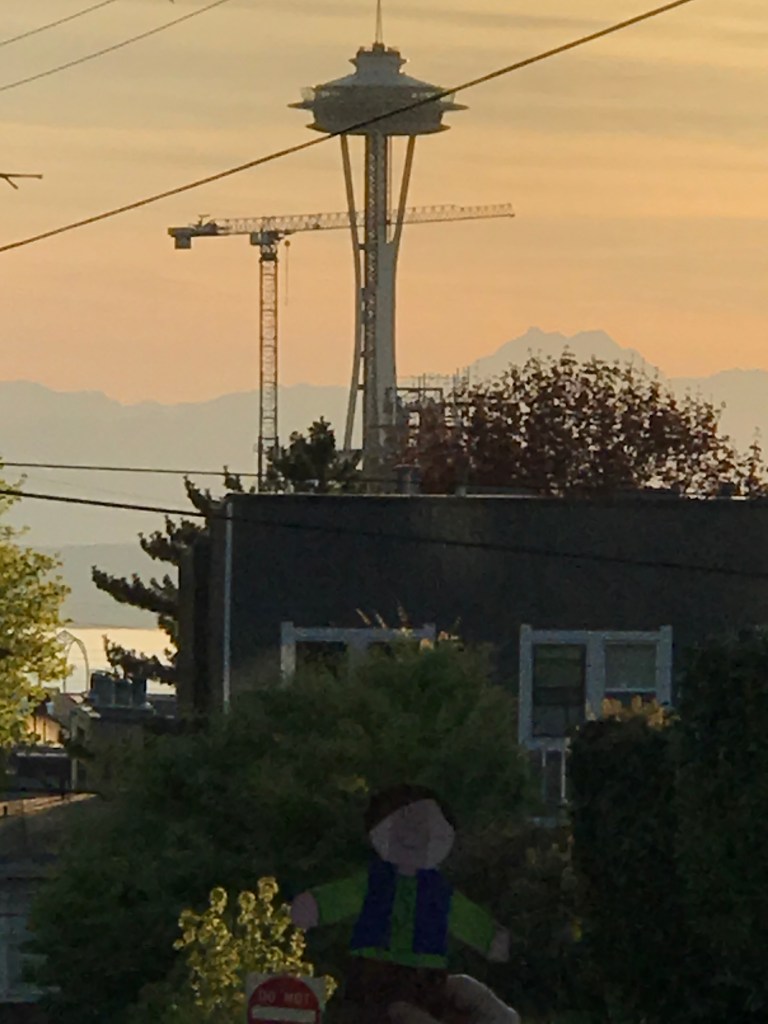 Paper cut out of a boy with Space Needle, crane, and mountain range in far distance. 