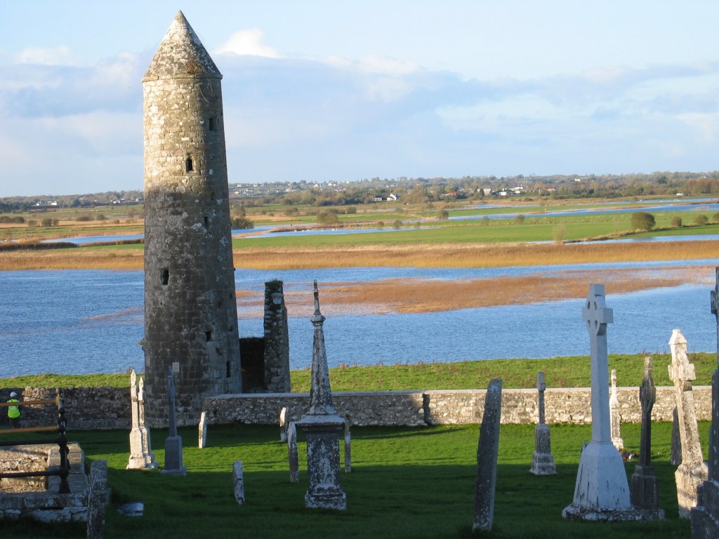 Old stone tower  in cemetery, Celtic crosses, River Shannon in distance. 
