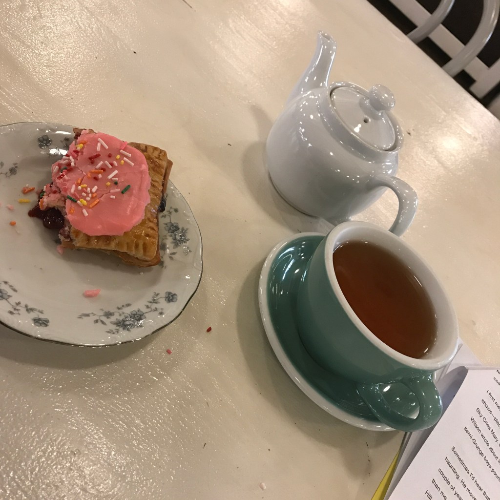 Teapot, full teacup, pastry on a flowered plate.