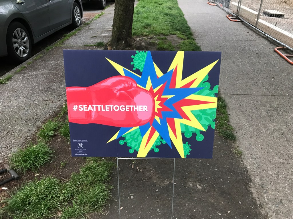 Sign on city street of red boxing glove punching Corona virus. 