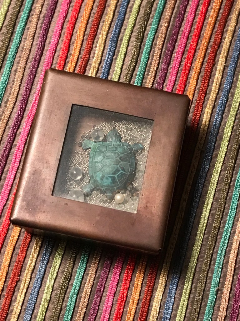 Copper box with with copper turtle, beads and glass balls surrounding it. 